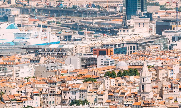 Vue panoramique de la ville de Marseille avec le Vieux-Port, ses bateaux et la célèbre basilique Notre-Dame de la Garde en arrière-plan.
