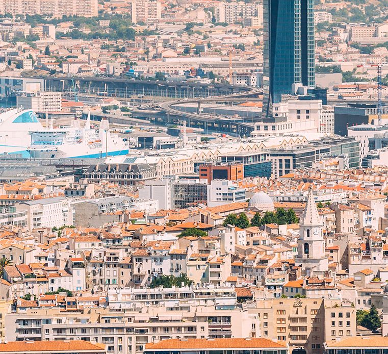 Vue panoramique de la ville de Marseille avec le Vieux-Port, ses bateaux et la célèbre basilique Notre-Dame de la Garde en arrière-plan.
