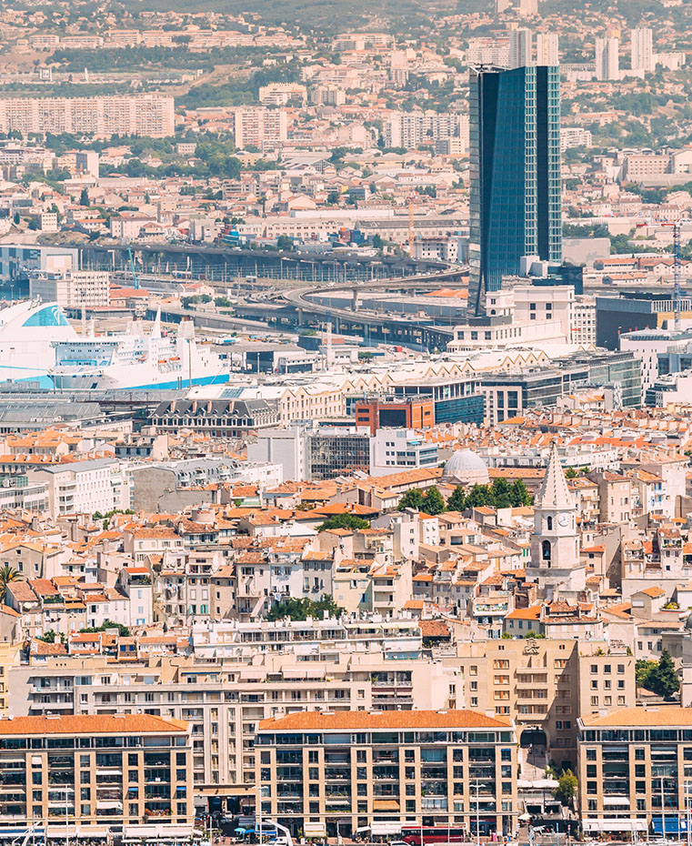 Vue panoramique de la ville de Marseille avec le Vieux-Port, ses bateaux et la célèbre basilique Notre-Dame de la Garde en arrière-plan.