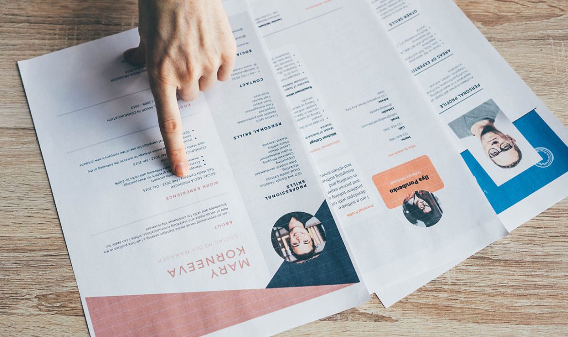 Un curriculum vitae posé sur une table, avec une main pointant vers une section spécifique. Le document contient des informations détaillées sur l'expérience professionnelle et les compétences.