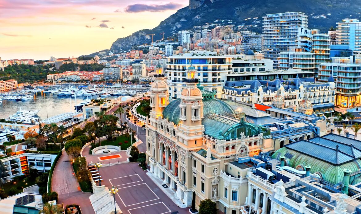 Vue panoramique sur Monaco, avec le Casino de Monte-Carlo au premier plan, des yachts dans le port et des bâtiments modernes s'étendant jusqu'aux montagnes en arrière-plan, parfait pour des enquêtes dans un cadre luxueux.